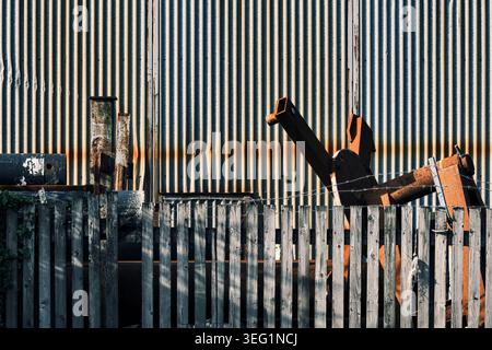Weathered wooden fence contrasting against a corrugated metal shed. The image features equally spaced parallel lines and a large, rusty metal object. Stock Photo