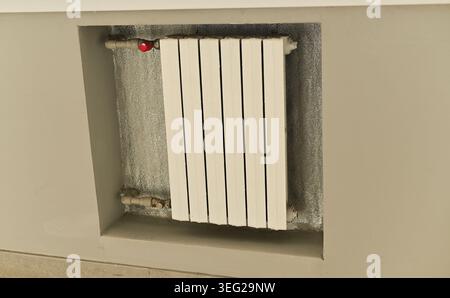 Wall-mounted radiator with white panels installed under window, indoor heating element providing warmth in modern interior, functional and practical d Stock Photo