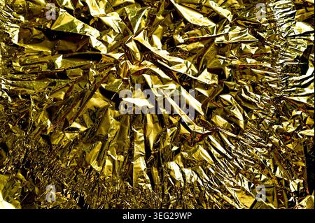foil texture in gold color with deep crumpled folds and sharp reflections, foil surface creating dynamic metallic pattern, bright highlights and shado Stock Photo