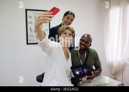 Happy diverse couple taking selfie with doctor holding ultrasound Stock Photo