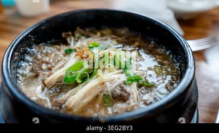 Close-up of a steaming Korean bulgogi soup served in a black stone pot, simmering broth with sliced beef, mushrooms, scallion, and sesame topping on a Stock Photo