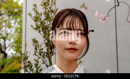 Close-up portrait of a young Japanese woman with an elegant traditional hairstyle and hair accessory, wearing a kimono and posing outdoors near soft s Stock Photo
