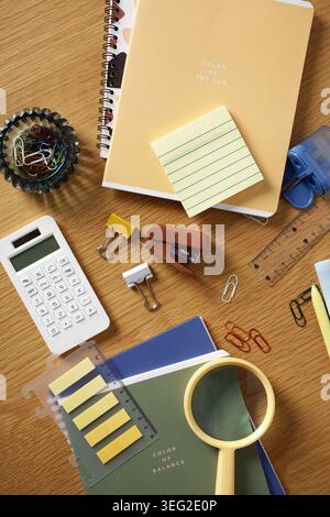 Contemporary home office flat lay with notebooks, sticky notes, calculator, binder clips, stapler, paperclips, ruler and magnifier on a wooden desk fo Stock Photo