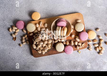 Colorful macarons in various flavors, including pistachio, are artfully placed on a wooden board with scattered pistachios, creating a delightful and Stock Photo