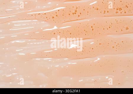 Abstract close-up of peach gel shower or shampoo texture with glossy streaks and tiny bubbles. Minimal cosmetic background for skincare, hygiene, spa, Stock Photo