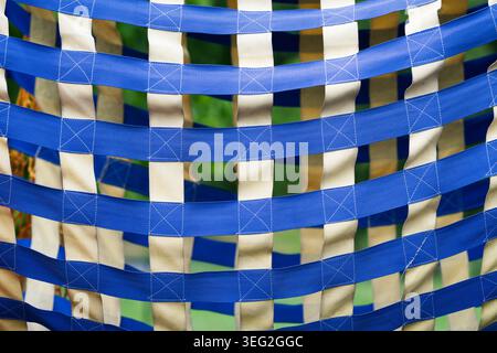 Close-up texture of a checkered net made of woven blue and beige nylon straps on a playground structure.  Abstract geometric background of blue and wh Stock Photo