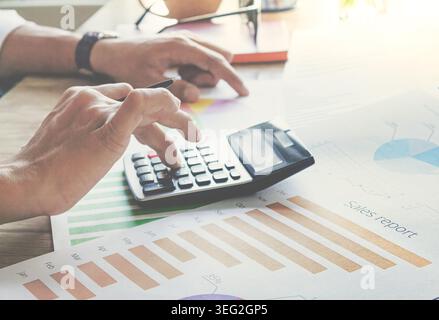 Hands press calculator keys over colorful bar graphs. Person focused, calculating financial data. Ideal for business, finance, or budgeting themes. Su Stock Photo
