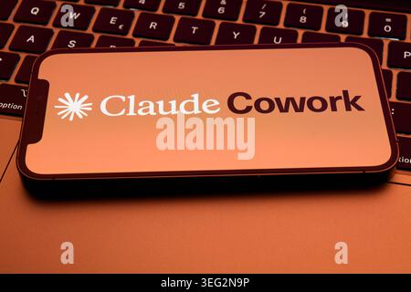 Claude Cowork Application Logo Displayed on Smartphone Resting on MacBook Keyboard Stock Photo