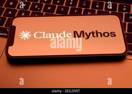 Claude Mythos Application Logo on Smartphone Resting on MacBook Keyboard in Warm Orange Tones Stock Photo
