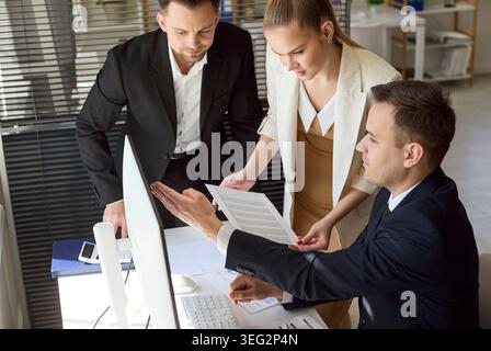 Business team of analysts reviewing data report at computer in office together Stock Photo