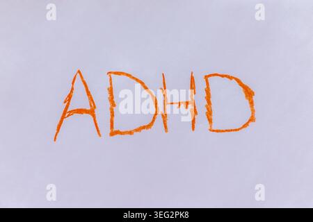 Close-up image of the word “ADHD” written in orange on a white background. It represents attention-deficit/hyperactivity disorder, mental health aware Stock Photo