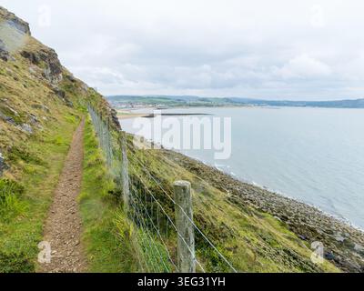 Hiking trail along Great Orme cliffs with panoramic views over Llandudno's West Shore bay, rugged coastline and distant town beneath a dramatic cloudy Stock Photo