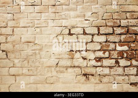 Old weathered brick wall with cracked white paint peeling off, revealing rough masonry texture beneath. Rustic distressed surface background. Stock Photo