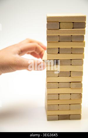A tower made of wooden bars, a game of gengo, stands on a white background, on the side the hand Stock Photo