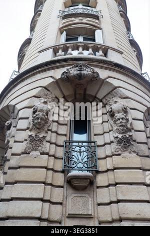 Dramatic low-angle view of a rounded corner tower on a classical Parisian building, featuring two expressive stone mascarons a serene female face and Stock Photo