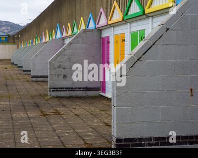 Row of brightly painted beach huts with contrasting white walls and angled concrete dividers standing along a seaside promenade, offering changing fac Stock Photo
