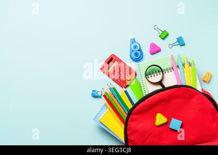 School backpack with stationery on blue background. Red backpack with notepads, pens, pencils and other stationery. Stock Photo