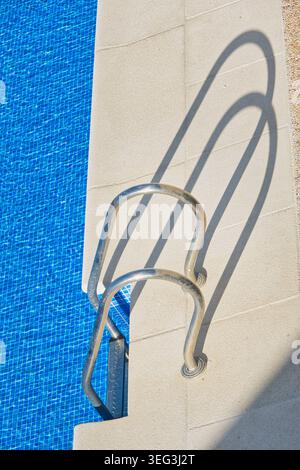 Metal ladder and blue tiled water in an outdoor swimming pool seen from above on a sunny day. Stock Photo