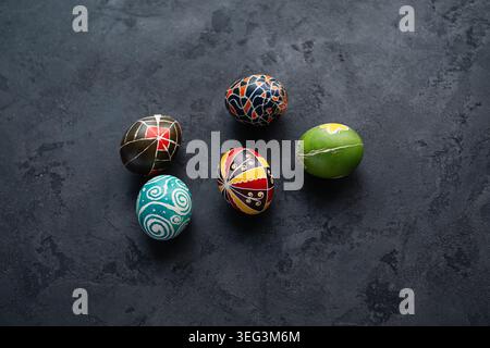 Five traditional Ukrainian Pysanky Easter eggs with geometric and floral patterns scattered on dark grey surface. Top-down view of hand-painted eggs. Stock Photo