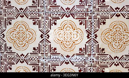 A high angle view of weathered ceramic tiles featuring intricate brown and yellow geometric patterns on a cream base. The aged surface shows natural c Stock Photo