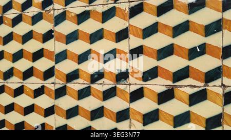 A close up of vintage ceramic tiles displaying a three dimensional geometric chevron design in black and orange. The weathered surface features visibl Stock Photo