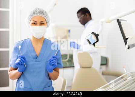 Female dentist standing in dental office with tools in hands Stock Photo