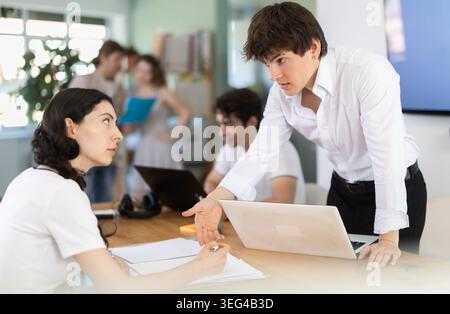 Several employees sit at desk during working day, working with laptop and paper documents. Stock Photo