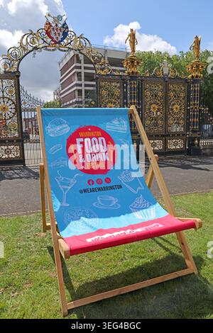 Festival-branded Warrington BID Food & Drink deckchair on Bank Park lawn before the Golden Gates of Town Hall, Warrington, in spring sun Stock Photo