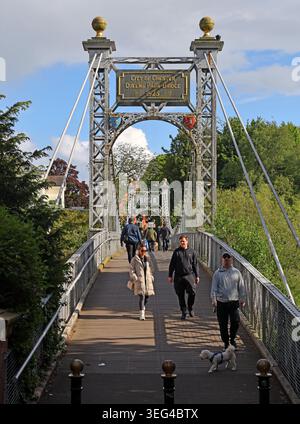 Summer pedestrians and a dog walker on the historic Queen’s Park suspension footbridge between The Groves and Handbridge, Chester. Stock Photo