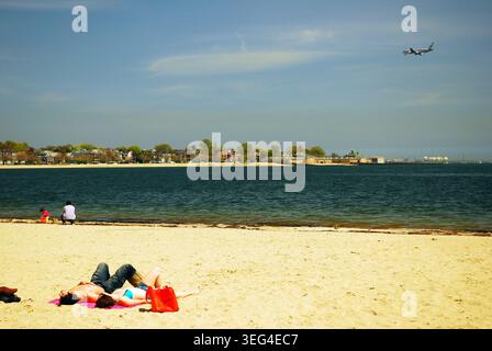 Boston, MA, USA May 5, 2008 A young adult couple relaxes on a beach in Southie, in South Boston, as an airplane comes in for a landing at Logan Airpor Stock Photo