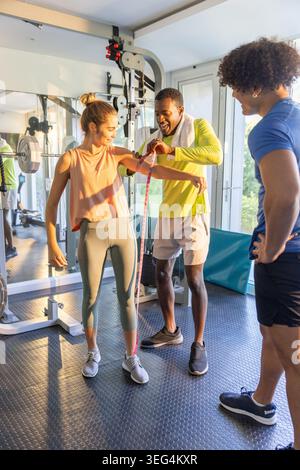 Diverse trainer and female client using measuring tape on upper arm in gym wearing sportswear Stock Photo