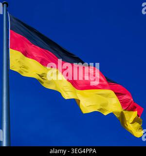 Close-up view of the German national flag waving in the wind against a deep blue sky on a sunny day. Square close-up image of the German national flag Stock Photo