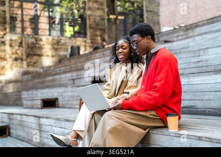 Positive smiling african american students man and woman relaxing after lessons outdoors together. Stock Photo