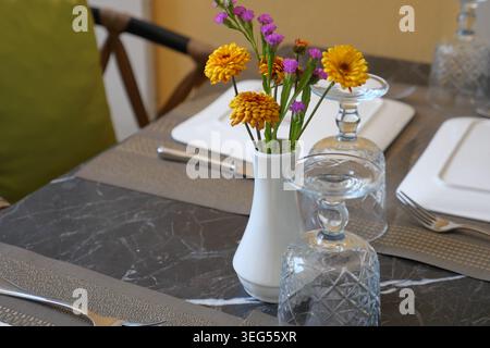 Flowers in a white vase on a dining table setting Stock Photo