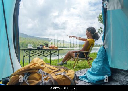 Young multiracial woman pointing at lake view from inside camping tent Stock Photo