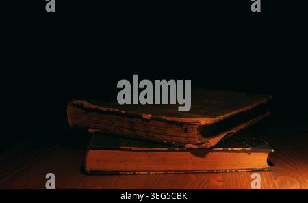 Stacked old worn literature books are sitting on a wooden table, creating a sense of history and mystery with warm light and dark shadows enhancing th Stock Photo