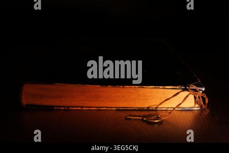 Old book with glowing pages and a vintage key lying on a dark wooden surface, representing the mystery and discovery of ancient knowledge and forgotte Stock Photo