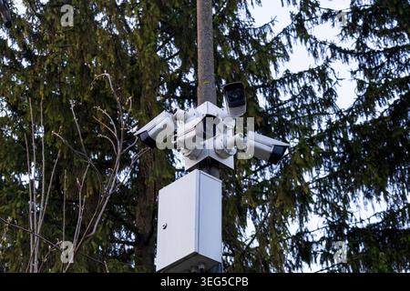 Multiple security cameras are installed on a pole, capturing the area amid trees. The devices are mounted for surveillance and safety purposes. Stock Photo