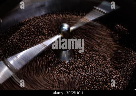 Highangle view of freshly roasted coffee beans being stirred by a rotating metallic arm inside an industrial cooling tray. Stock Photo