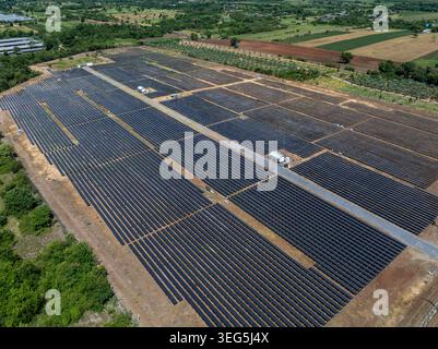 A highangle view of a largescale commercial solar farm featuring rows of photovoltaic panels in a rural landscape for sustainable energy production. Stock Photo