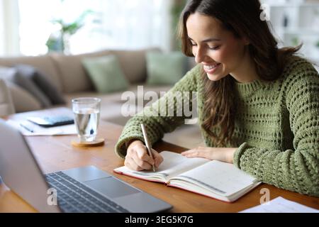 Happy teleworker writing in paper agenda working in a house interior Stock Photo