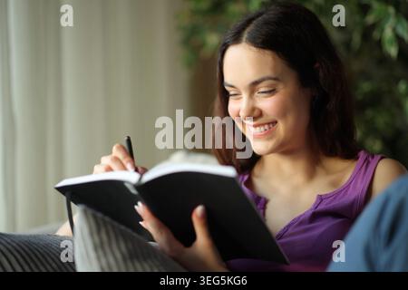 Happy young woman writing notes in paper agenda sitting on a couch at home Stock Photo