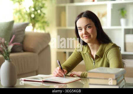 Satisfied young woman writing in agenda looks at you at home Stock Photo