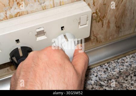 A man's hand inserts a plug into a socket. Sockets in the wall, wires in the socket on the kitchen wall, overloaded wall sockets, home fire safety con Stock Photo