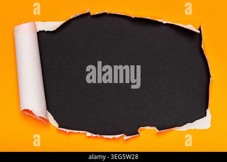 A vibrant orange paper is torn open, revealing a textured black surface underneath. Stock Photo