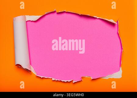 A piece of vivid orange paper torn open to reveal a bright pink surface underneath. Stock Photo