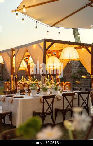 Elegantly Set Outdoor Dining Table with Romantic String Lights and Floral Centerpiece at Dusk Stock Photo