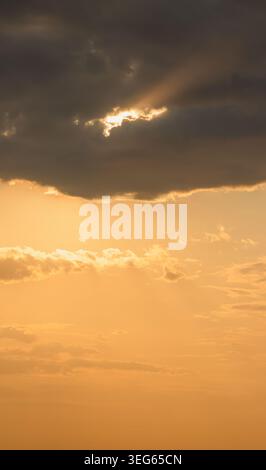 Golden sunbeams bursting through dark, dramatic clouds, creating a vibrant warm glow across the sky, symbolizing hope, spirituality, and change at gol Stock Photo