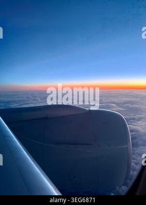 View from an airplane window over the North Atlantic Ocean with the sun rising over the horizon.  Airplane engine and wing in view.  No people Stock Photo