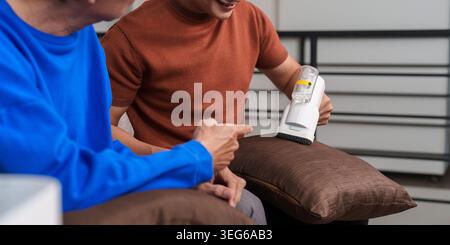 Asian son helping senior father with home cleaning using lint remover. Stock Photo
